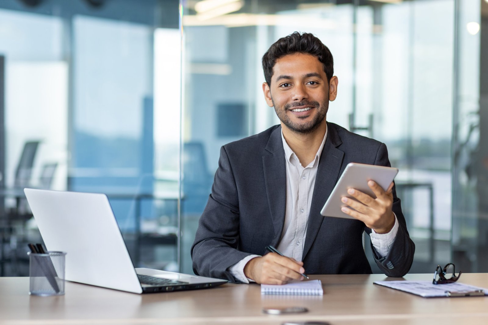 Portrait of young businessman with tablet computer inside office, hispanic man smiling and looking at camera, working with laptop, using app on tablet