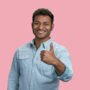 Young smiling south asian man showing a thumb up. Happy successful guy giving his like. Isolated on pink background.