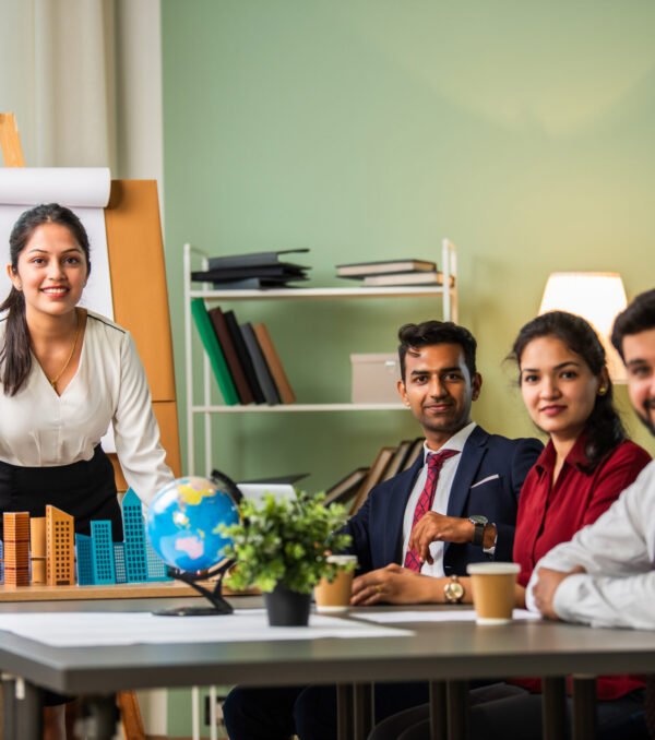 Asian Indian leader in 30s coaching interested business people, giving educational workshop presentation in office. Concentrated employees listening to professional coach at workshop.